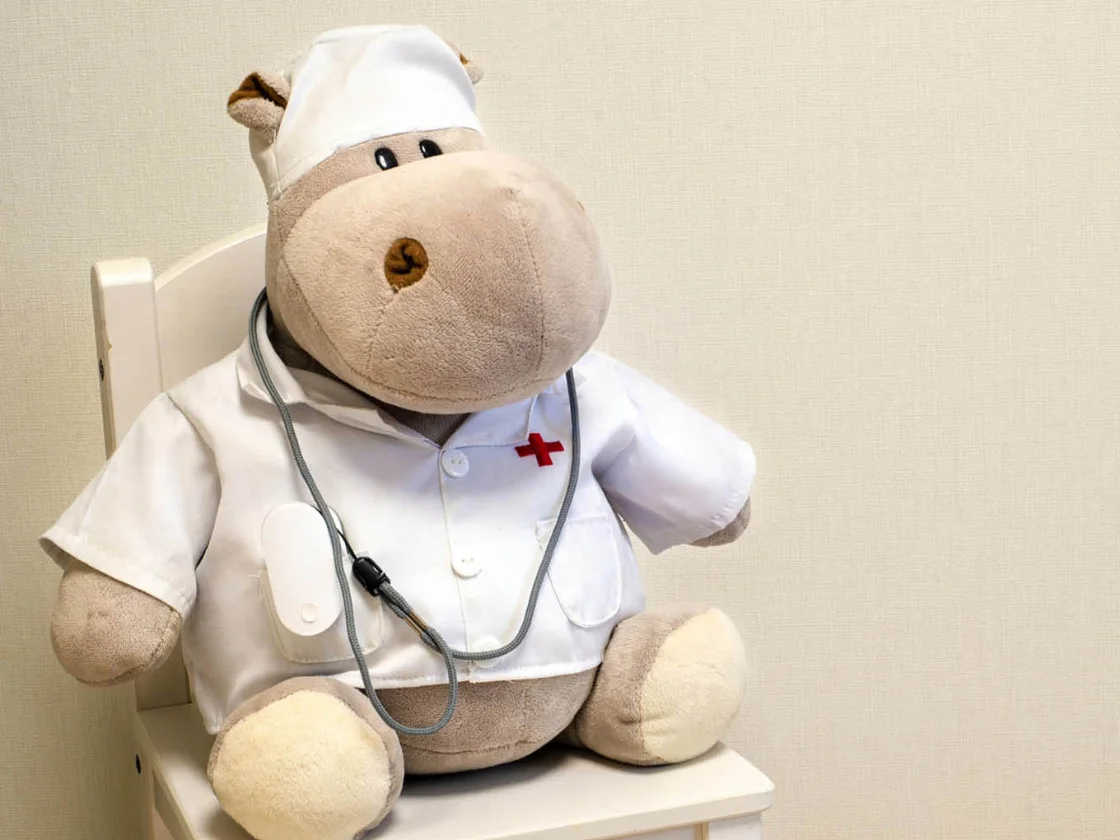 Plüsch-Nilpferd im Arztkittel mit Stethoskop auf einem Kinderstuhl